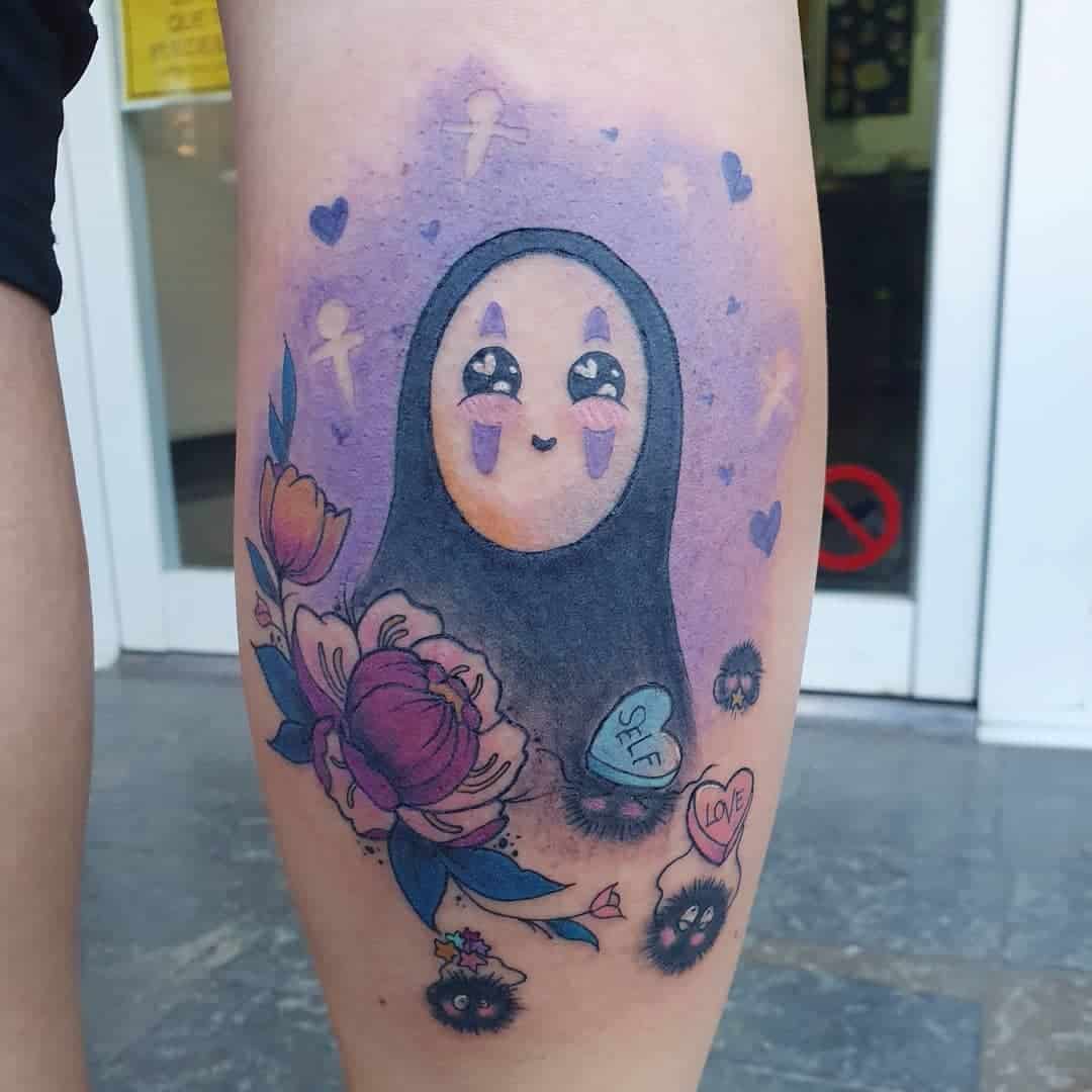 Colorful tattoo of No-Face from Spirited Away, surrounded by flowers, soot sprites, and candy hearts with words 'self' and 'love'