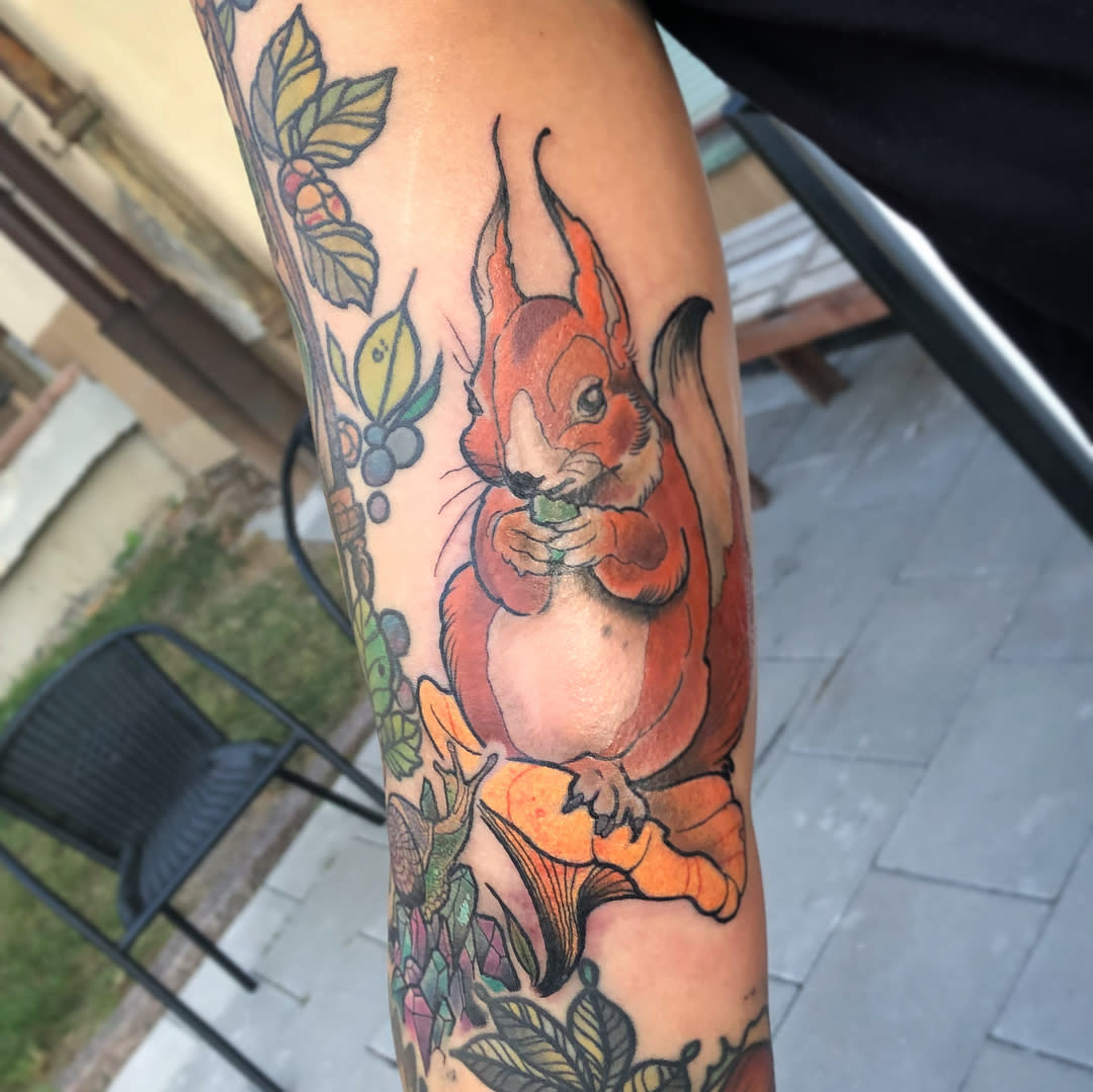 Tattoo of a red squirrel eating a nut, surrounded by floral designs on an arm