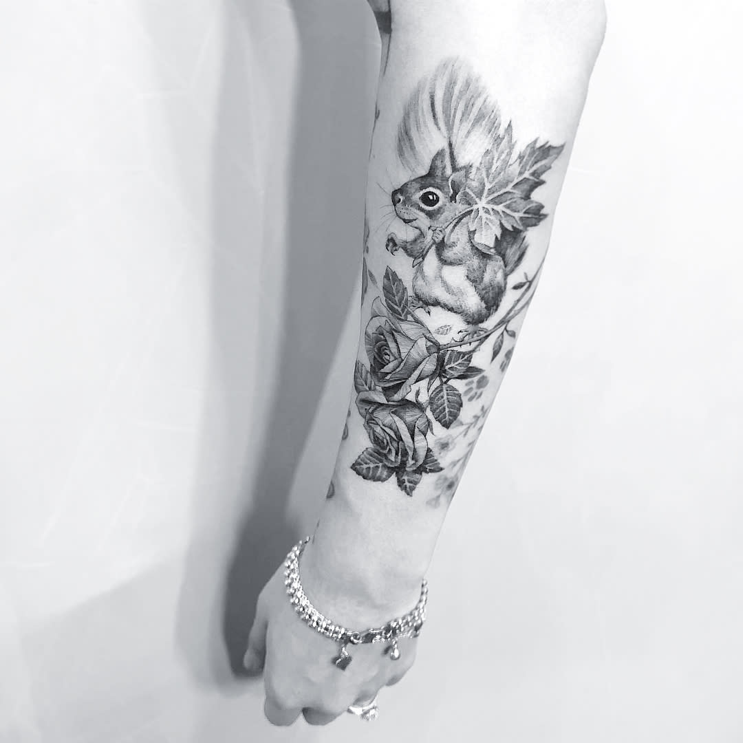 Forearm tattoo with a detailed squirrel and flowers in a black and gray color scheme