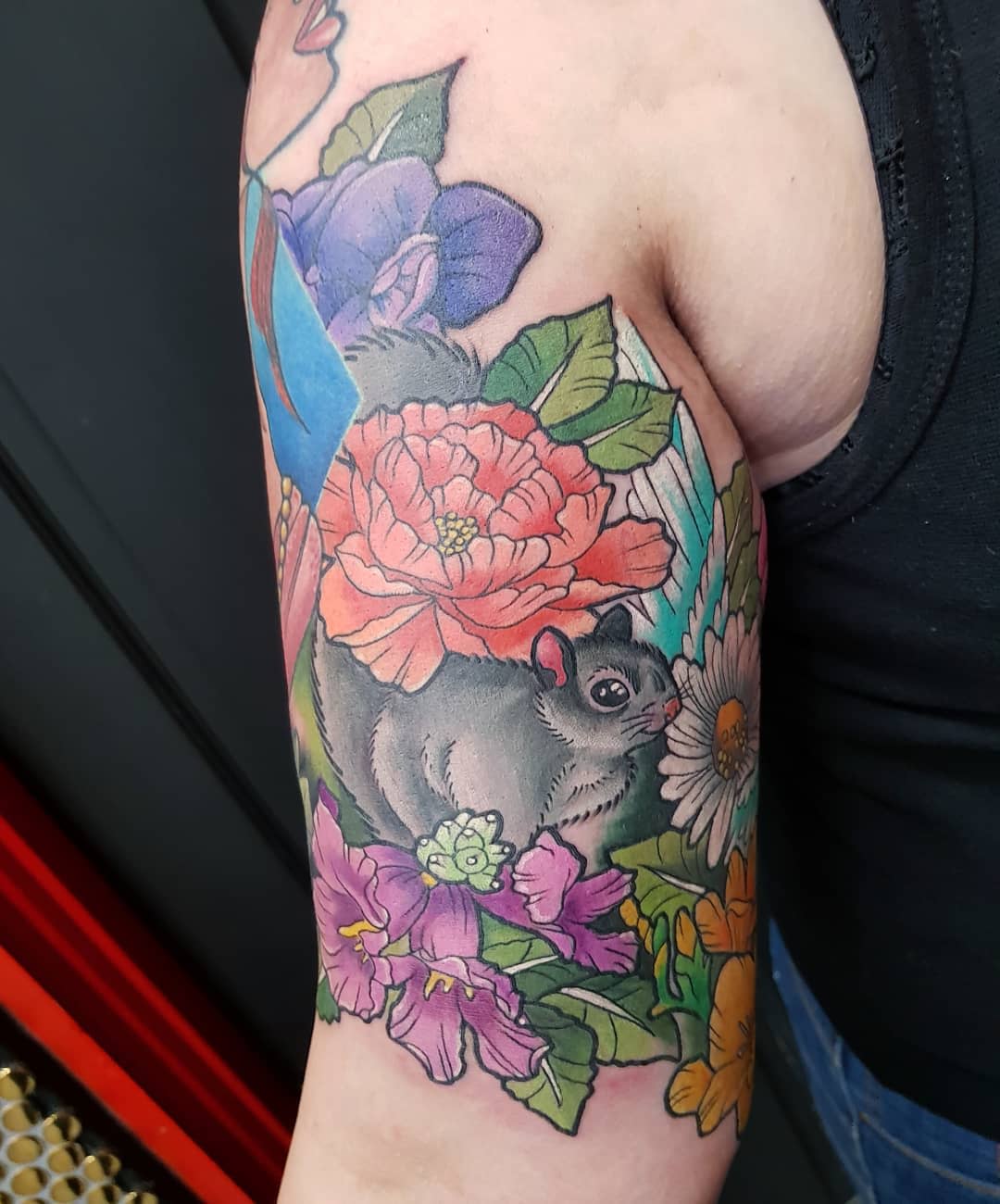 Colorful tattoo of a squirrel with flowers on an upper arm