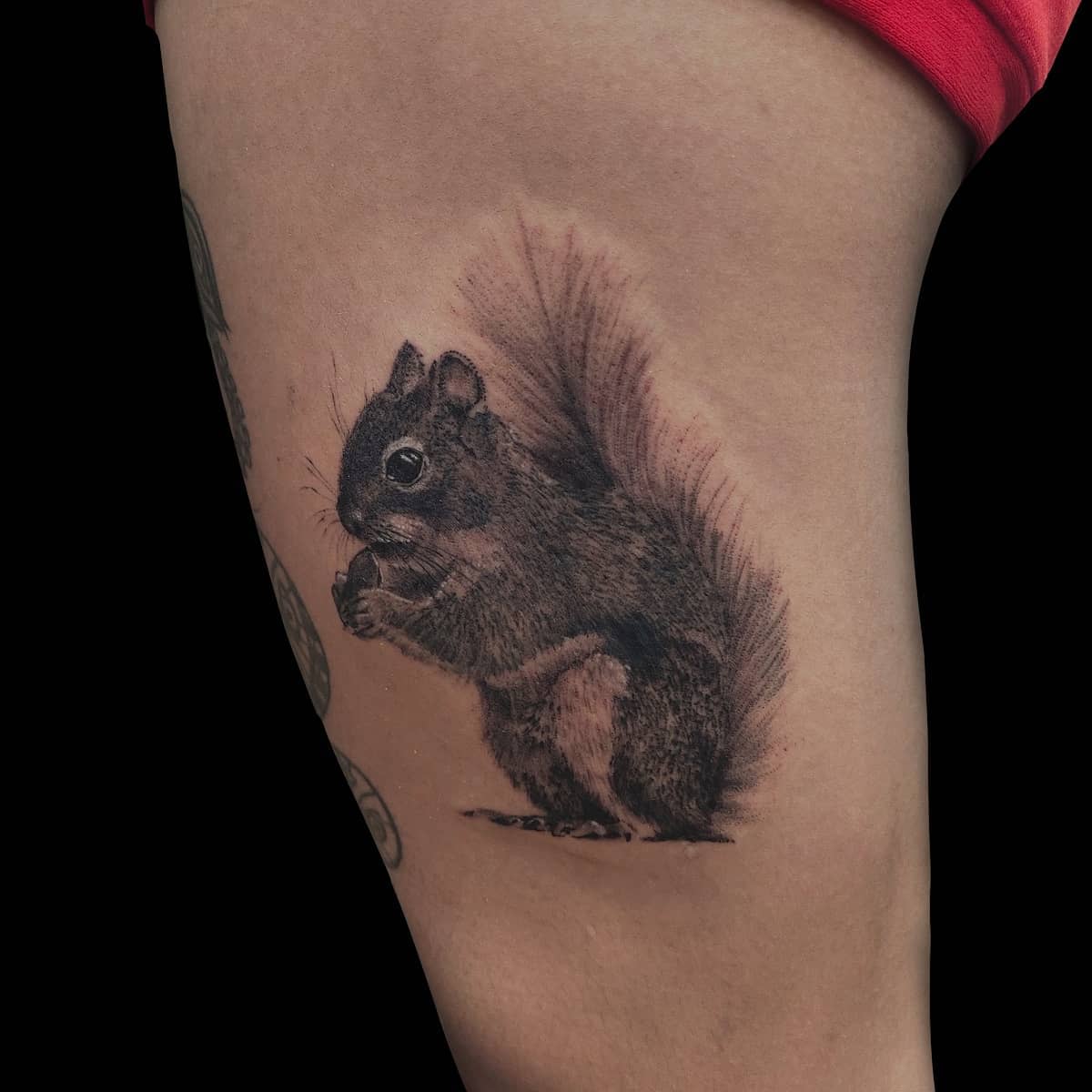 Tattoo of a realistic squirrel eating a nut, placed on an arm