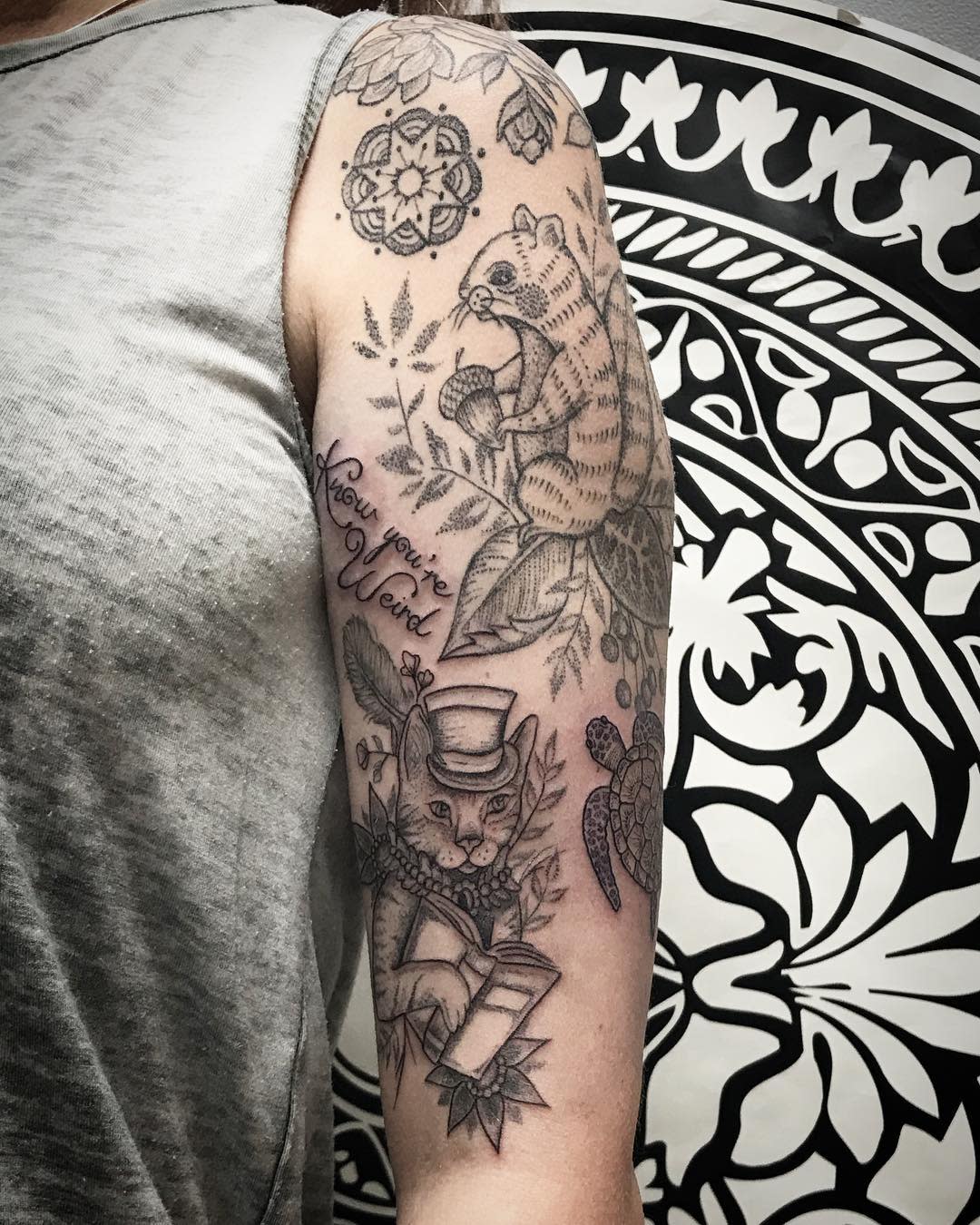 Arm tattoo featuring a raccoon, a cat in a hat reading a book, leaves