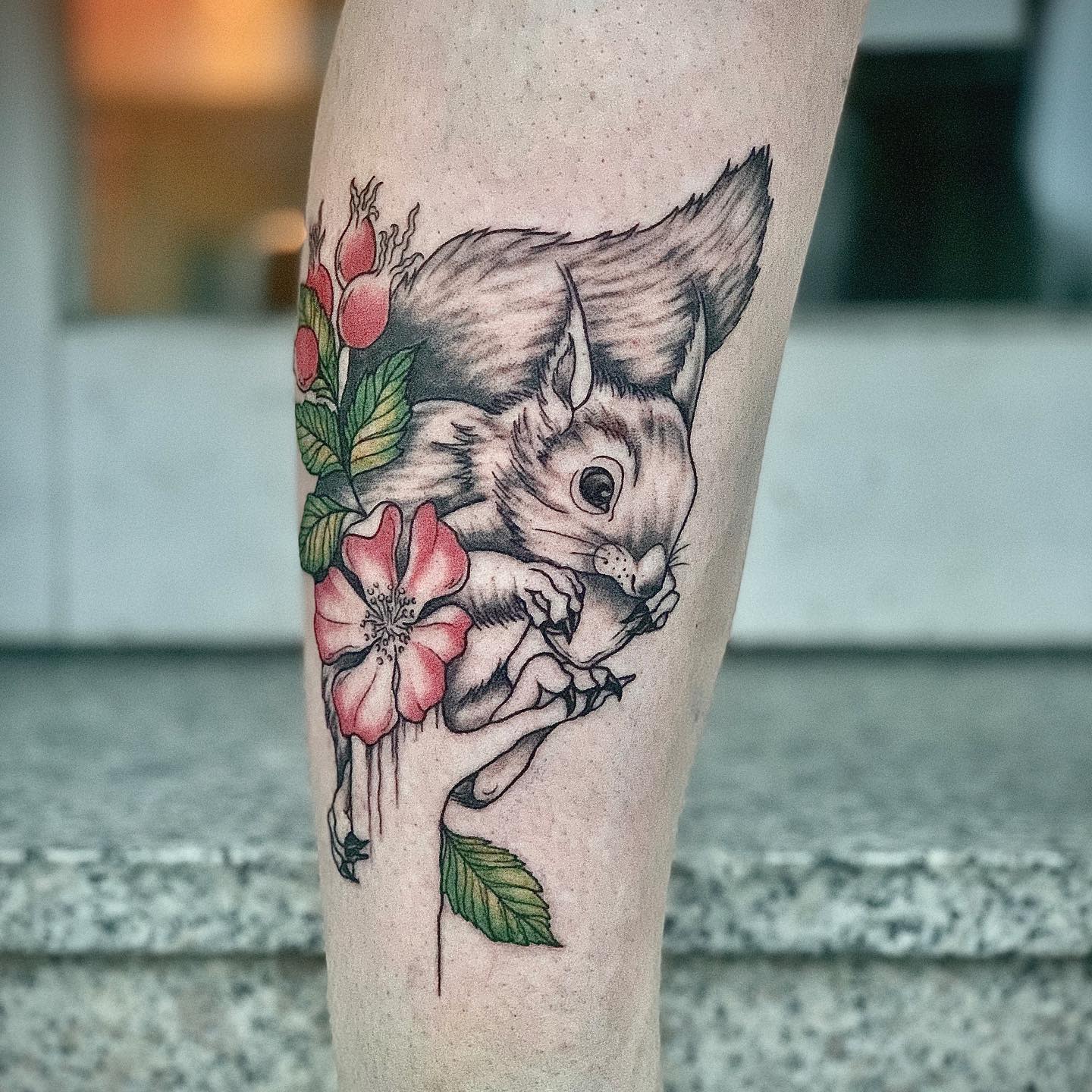 Tattoo of a squirrel with a flower and leaves on a leg