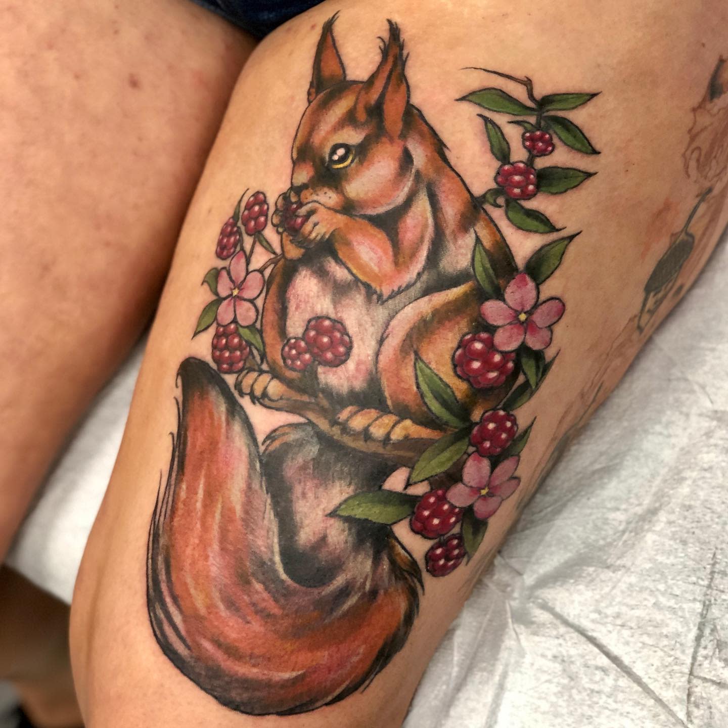Tattoo of a squirrel with berries and flowers on an upper thigh