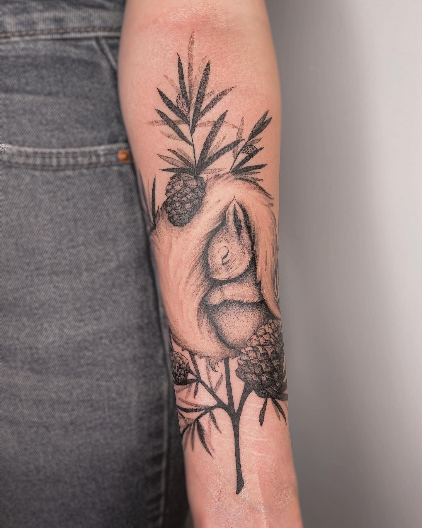 Tattoo of a curled-up squirrel among branches and pinecones on the inner forearm