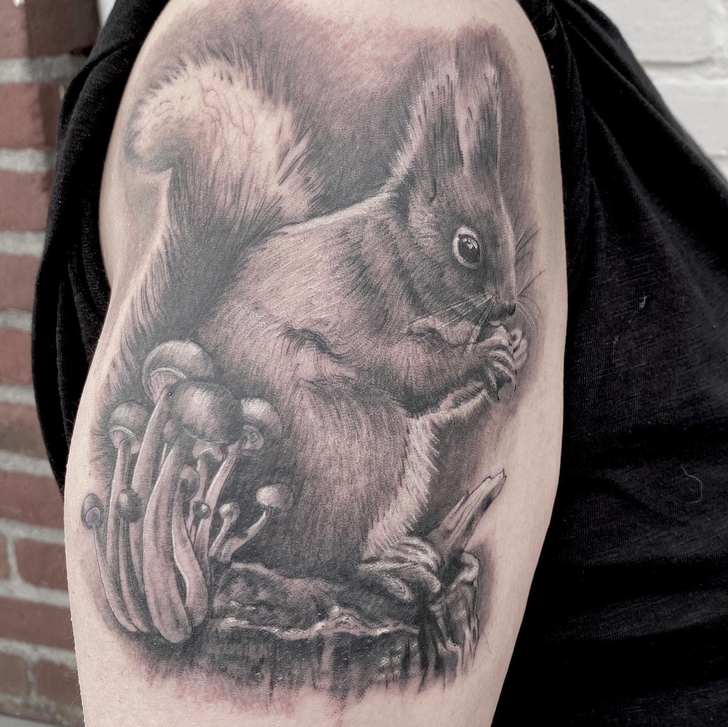A detailed tattoo of a squirrel sitting by mushrooms on an upper arm