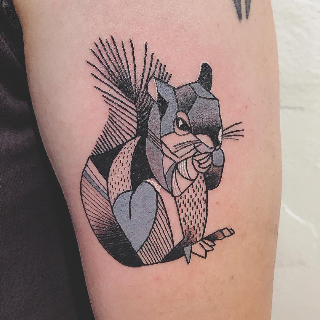 Geometric tattoo of a squirrel on an upper arm composed of black, gray, and blue shapes