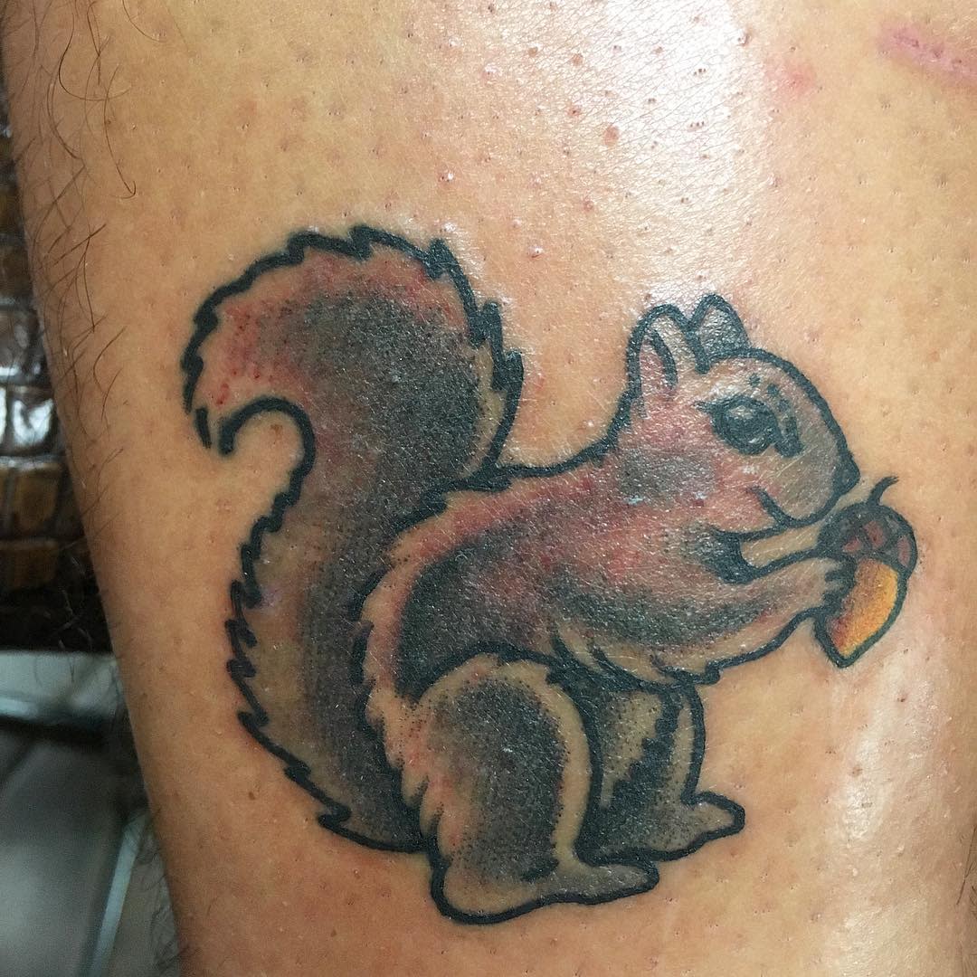 Tattoo of a squirrel holding an acorn on skin