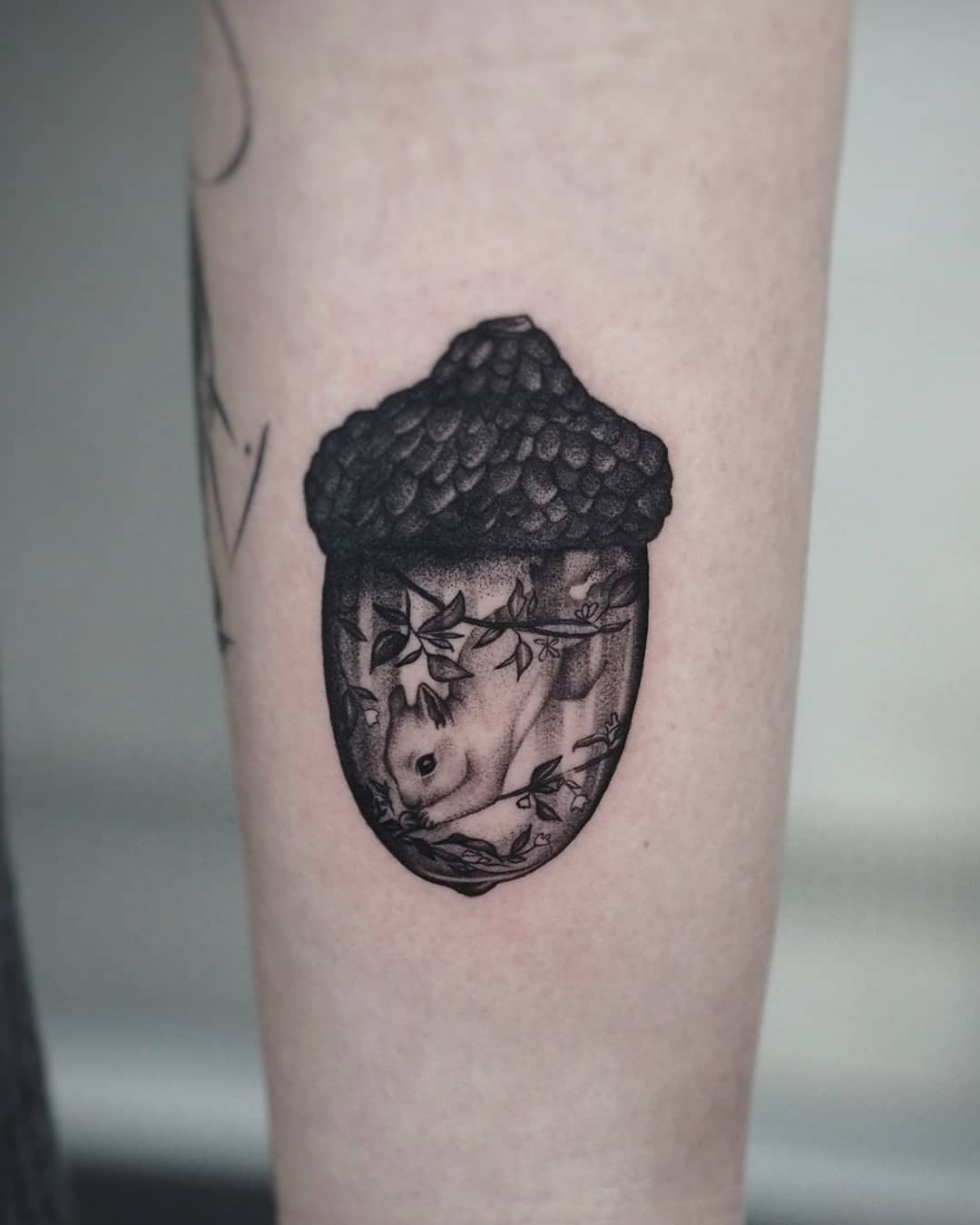 Tattoo of an acorn with a detailed black and white portrait of a squirrel inside