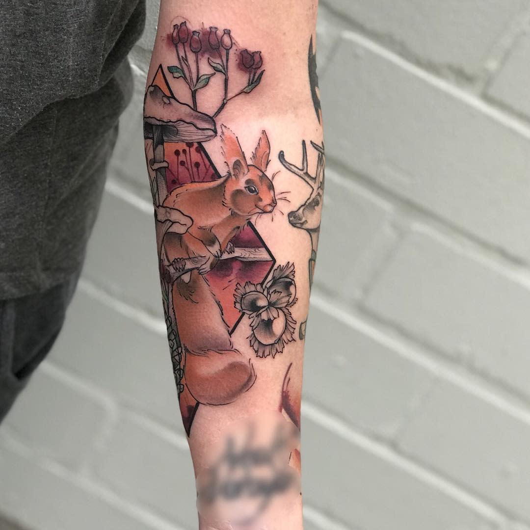 Forearm tattoo featuring a rabbit, deer, flowers, and a mountain landscape in vibrant colors