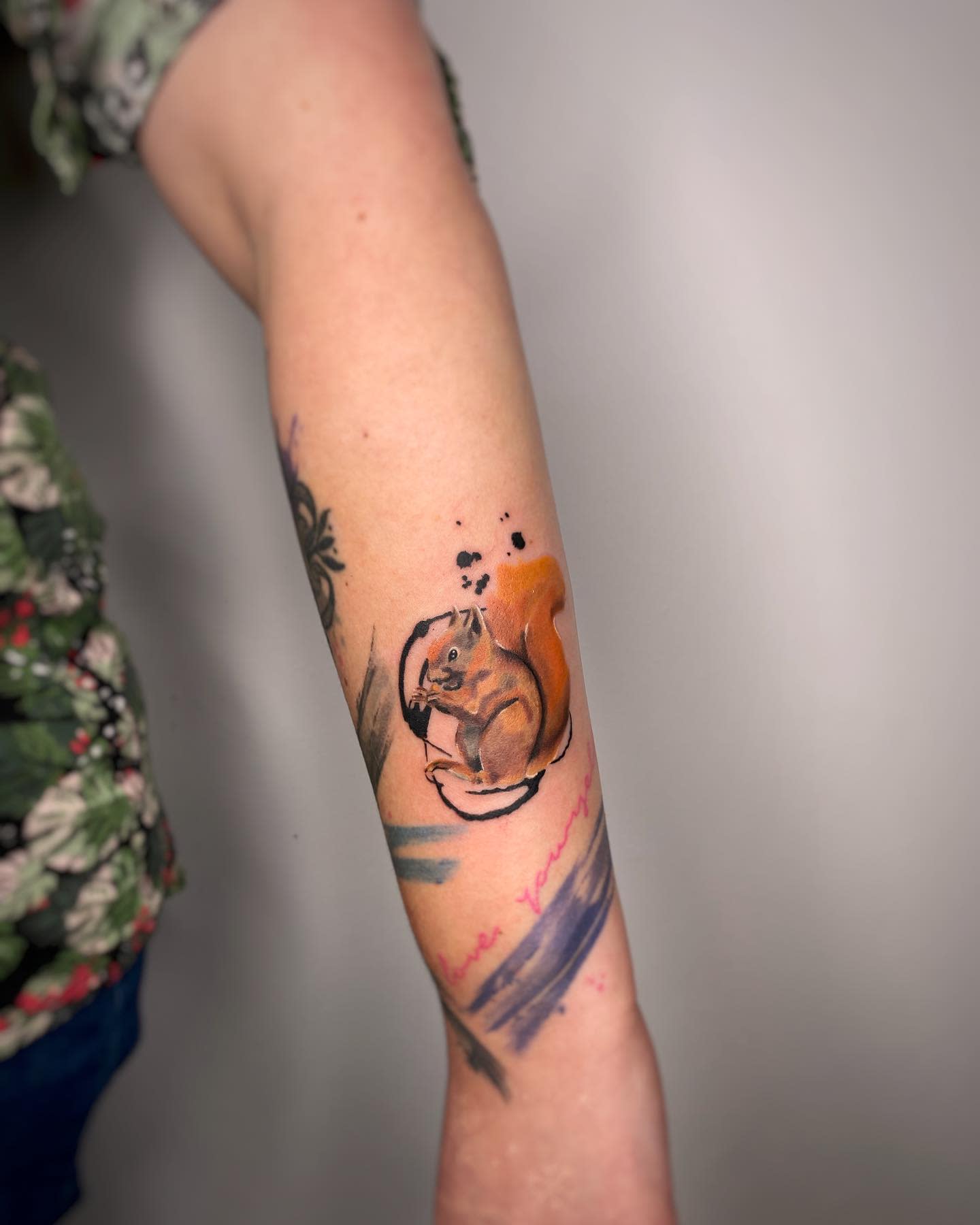 Tattoo of a squirrel holding a teacup on a forearm with colorful accents around