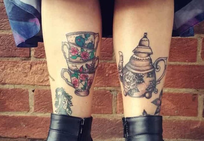 Colorful tattoo of three stacked floral teacups on one leg and a vintage teapot with roses on the other, creating a tea-themed design