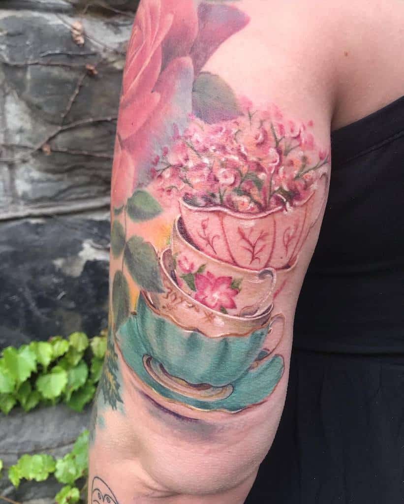 Colorful tattoo of stacked vintage teacups with delicate floral patterns, pastel colors, and tiny pink flowers blooming from the top
