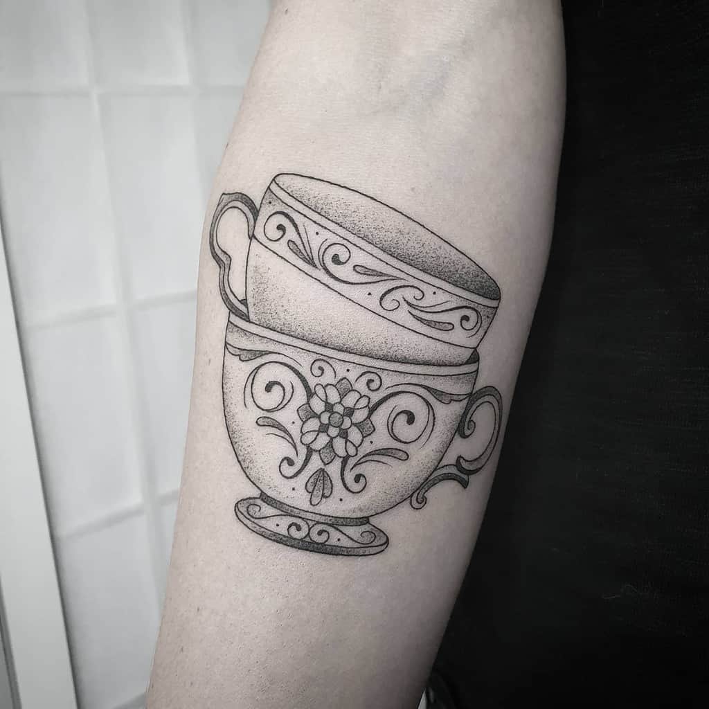 Tattoo of two intricately designed teacups stacked, featuring floral and swirl patterns