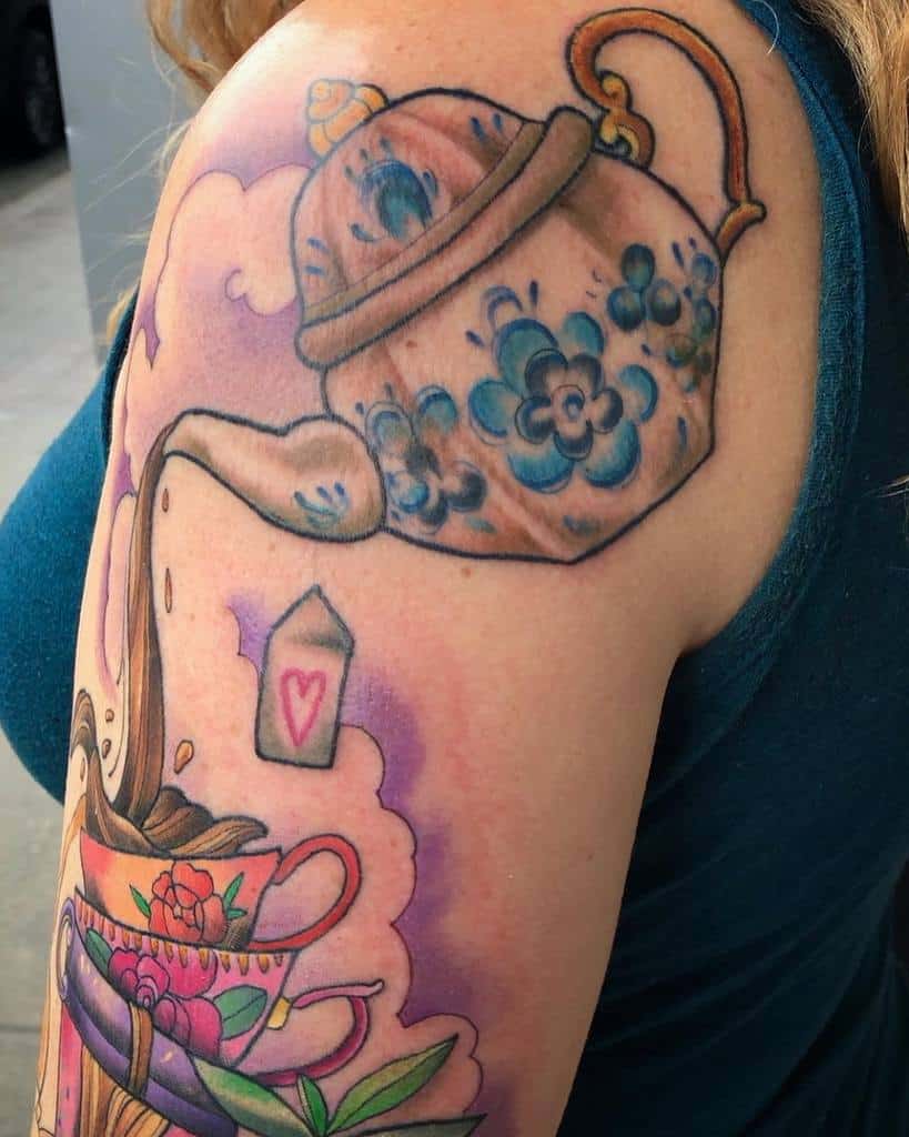 Colorful tattoo of a vintage blue floral teapot pouring tea into stacked teacups with vibrant patterns, a teabag, and steam details