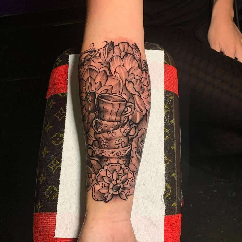 Black and grey tattoo of stacked teacups with floral patterns, surrounded by detailed blooming flowers and intricate shading