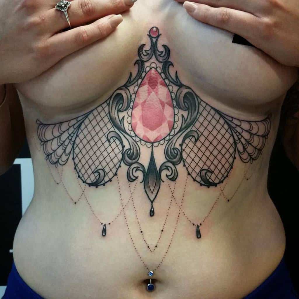 Decorative chandelier tattoo with lace patterns, intricate swirls, and a central pink gem-like design, with dangling dotted lines with beads