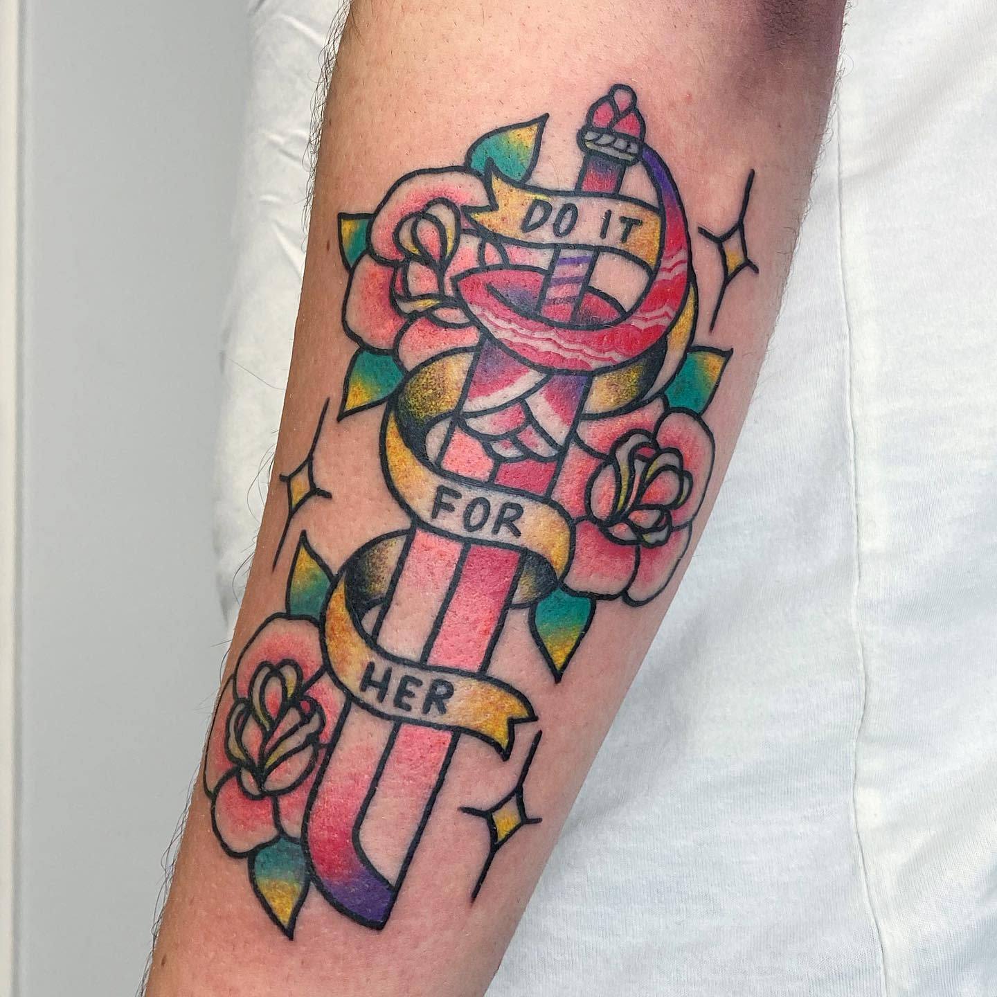 A vibrant Steven Universe tattoo featuring Rose Quartz's sword wrapped with a banner that reads 'Do it for her,' accented with pink roses and sparkling stars on the arm