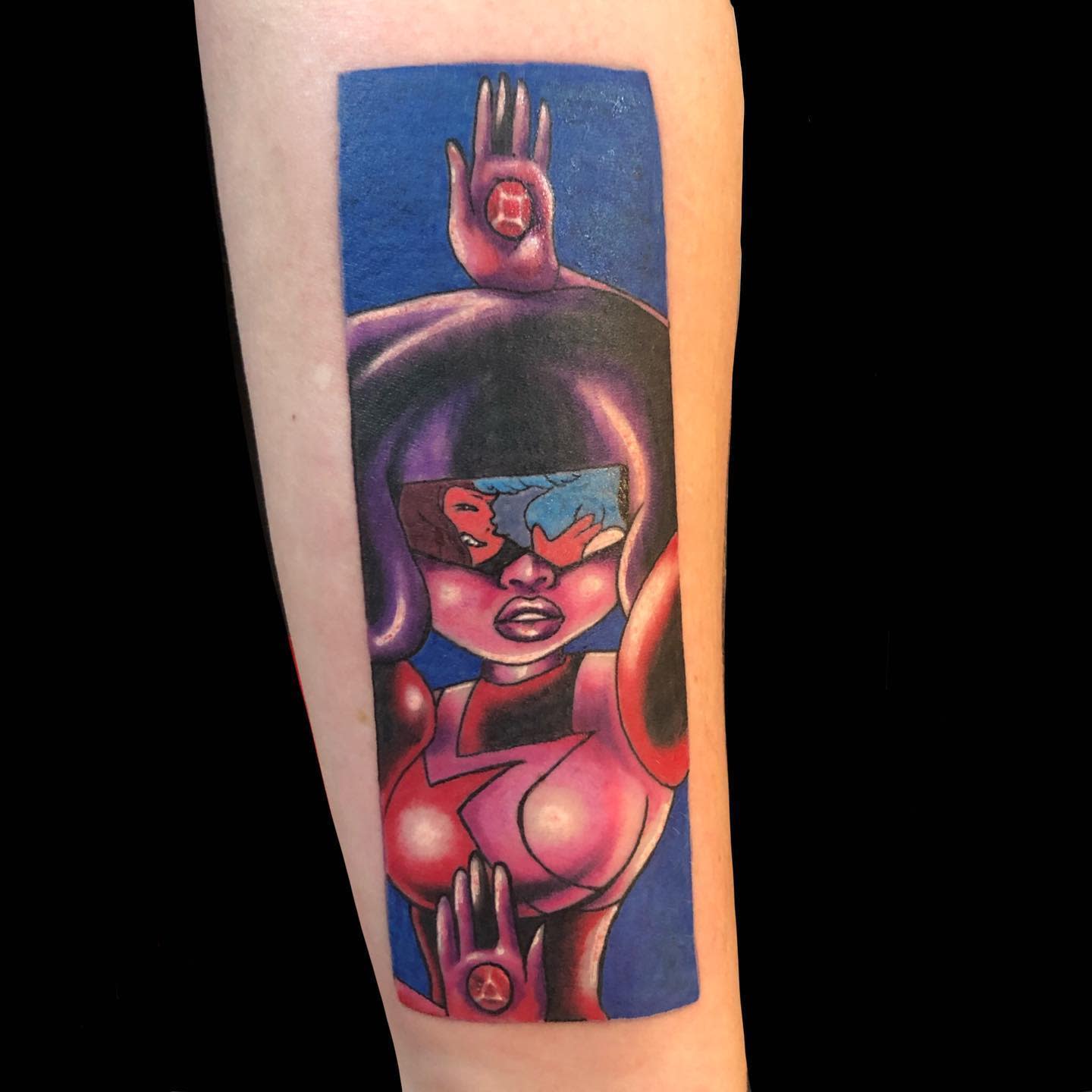 Bold and colorful tattoo of Garnet from Steven Universe, with her hands raised, displaying gemstones, and a reflection of Ruby and Sapphire in her visor, on the forearm