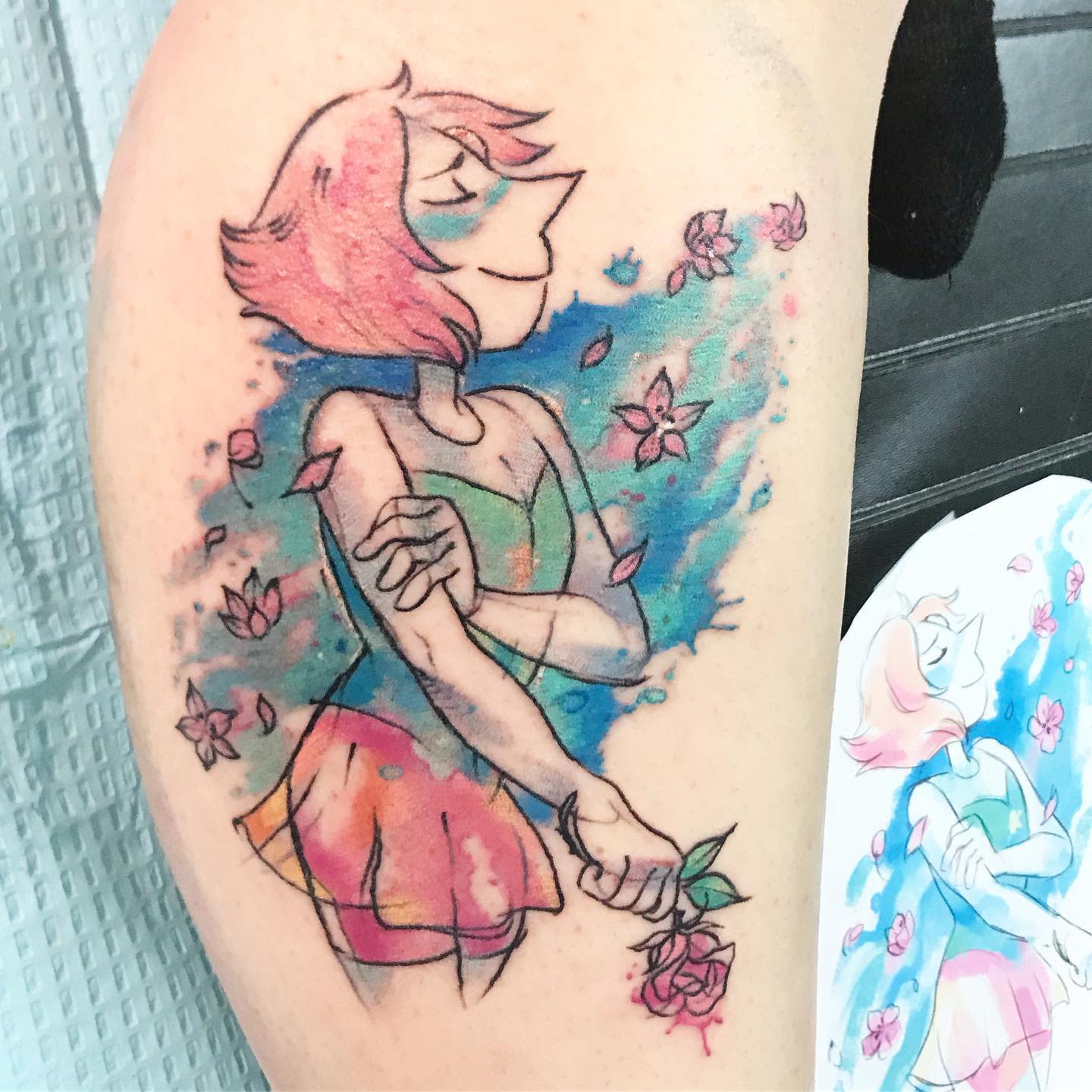 Colorful tattoo of Pearl from Steven Universe, depicted with a peaceful expression, holding a rose and surrounded by floating petals, on the upper arm