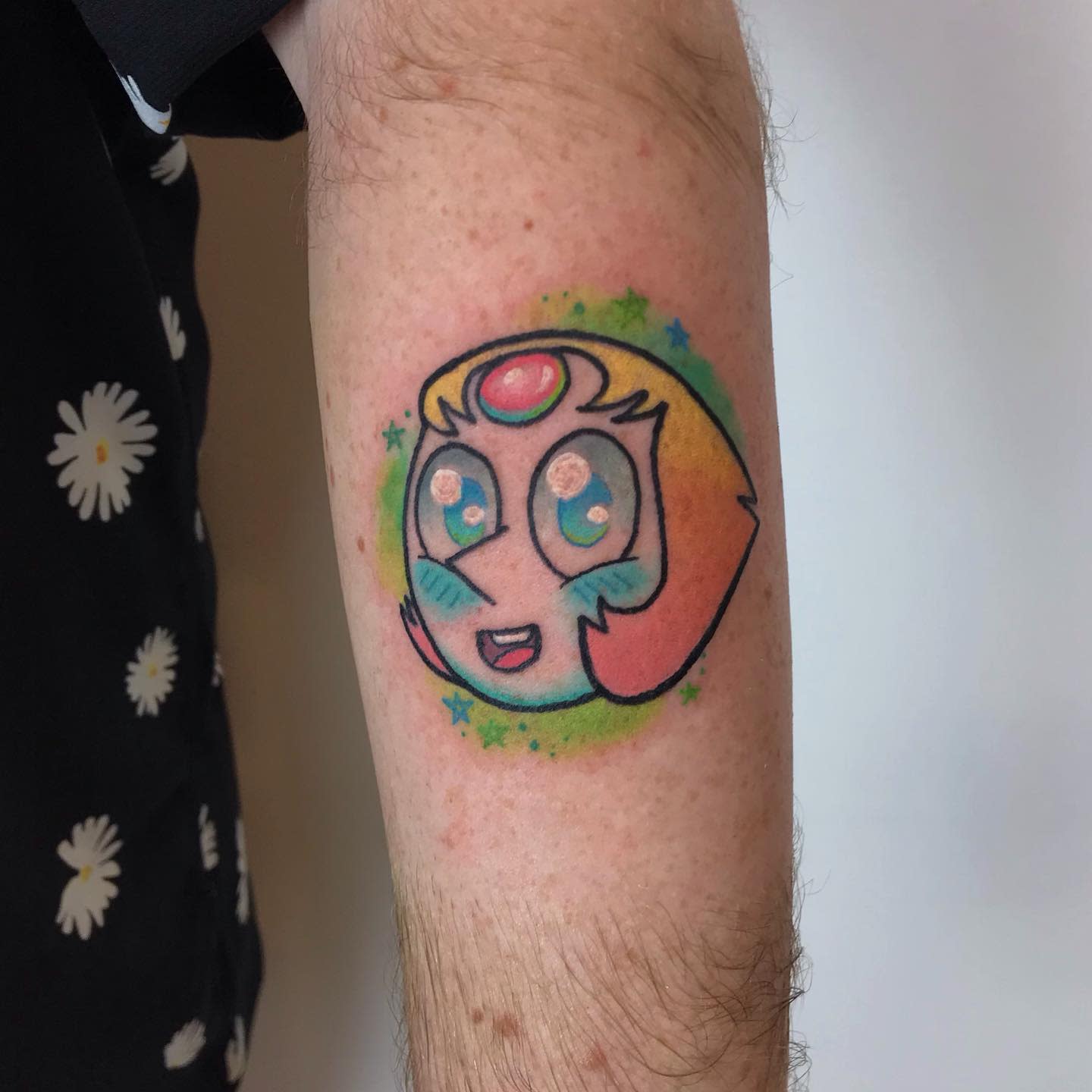 Chibi-style tattoo of Pearl from Steven Universe with large, sparkling eyes, surrounded by colorful stars, on the forearm