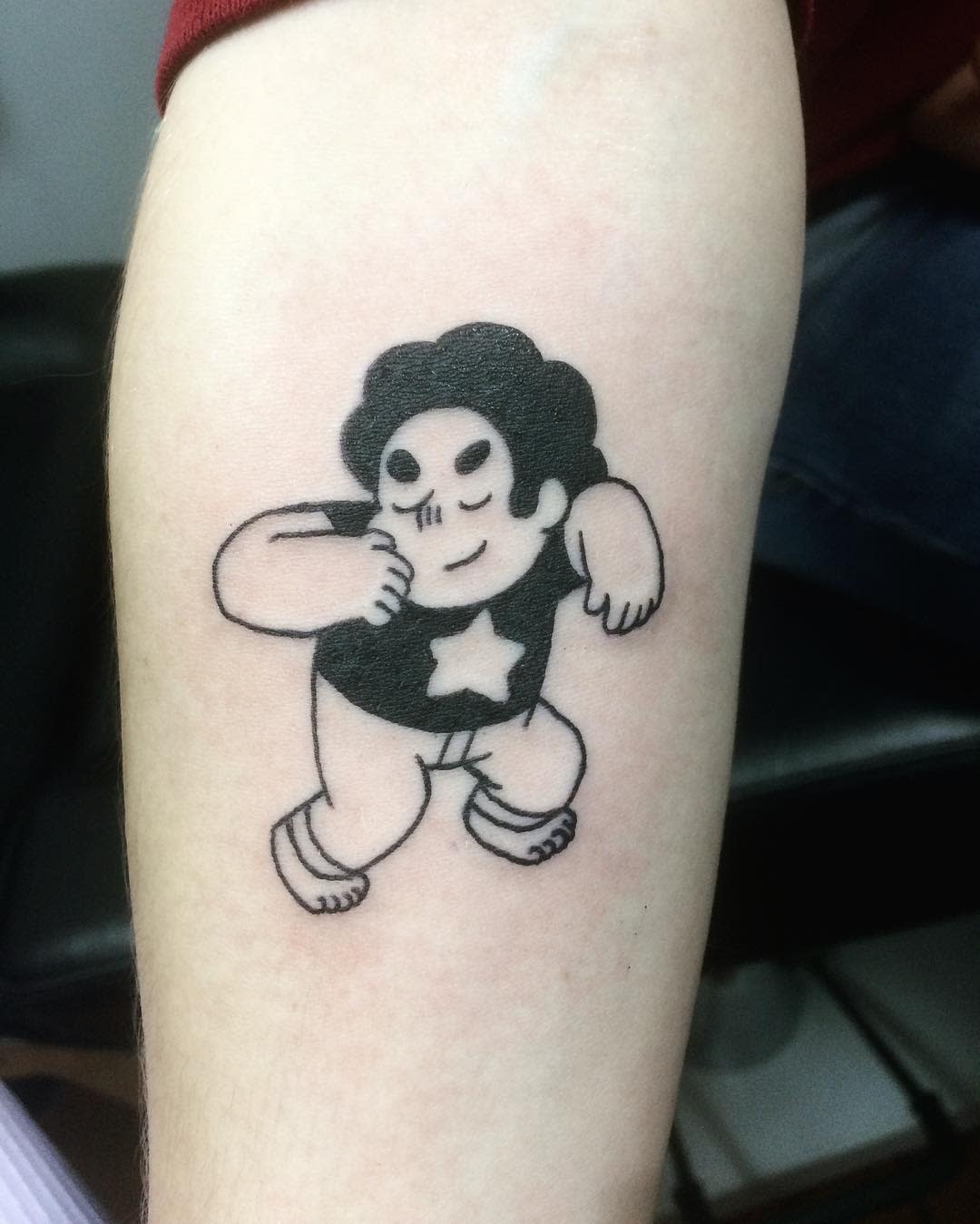 Simple black ink tattoo of Steven Universe in a confident pose, on the upper arm
