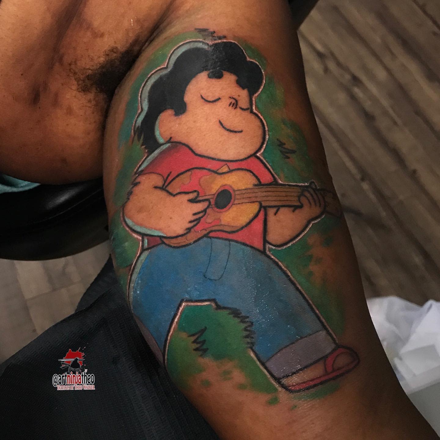 Vibrant tattoo of Steven Universe playing a ukulele, smiling with eyes closed, on the upper arm