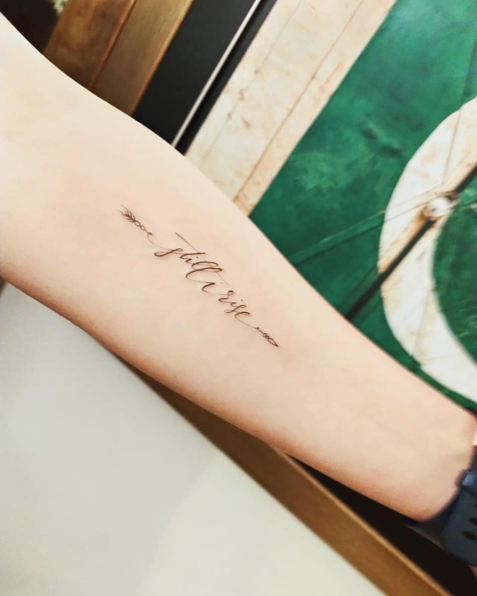 Arm with "still i just rise" tattoo in cursive, flanked by arrows