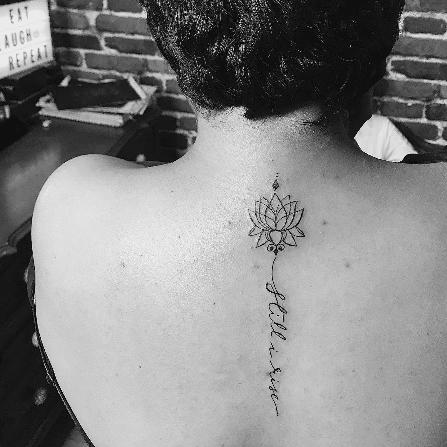 Black and white image of a back with a lotus tattoo and cursive "still I rise" text
