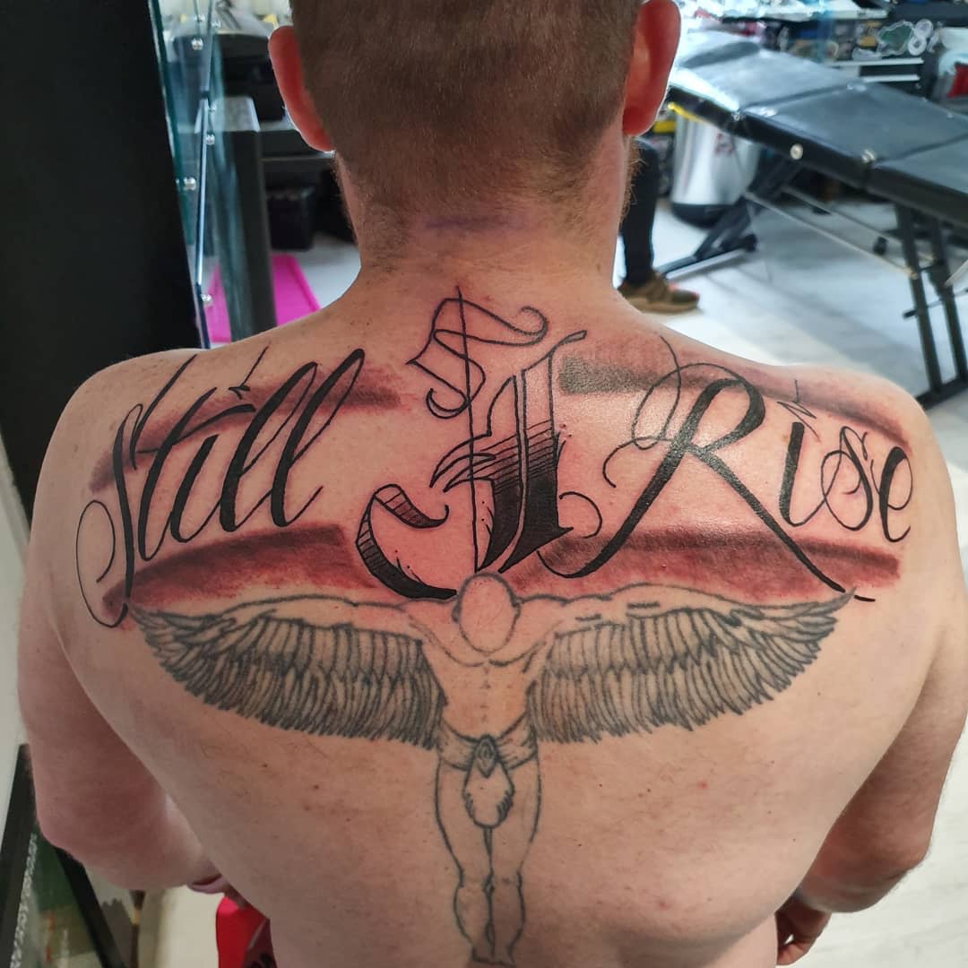 Back tattoo featuring the phrase "Still I Rise" along with a detailed image of a winged figure with outstretched arms