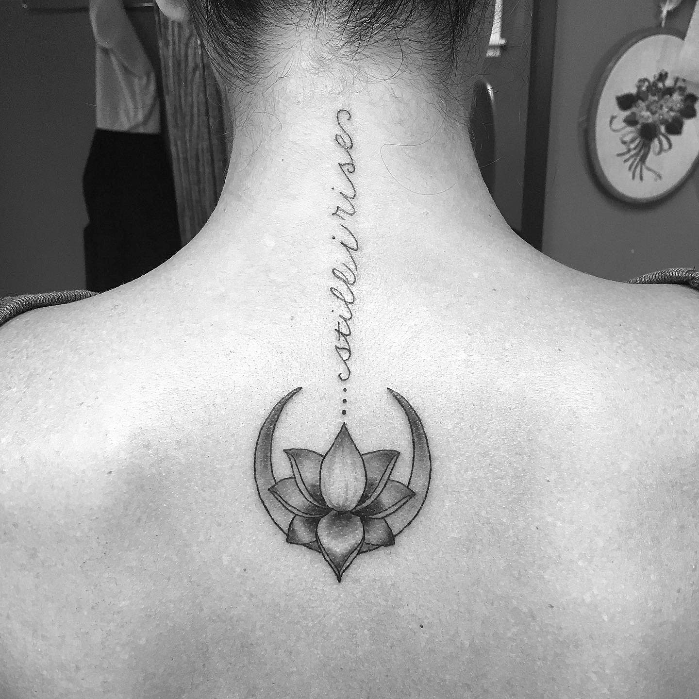 Black and gray lotus flower tattoo with script "still I rise" on upper back