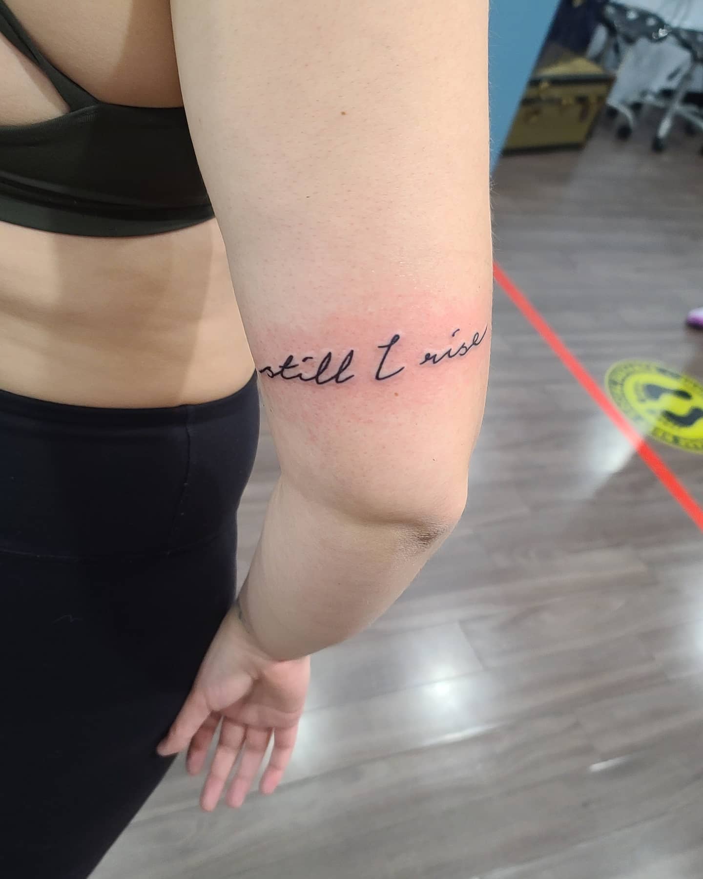 A tattoo on an inner arm reads "still I rise" in cursive