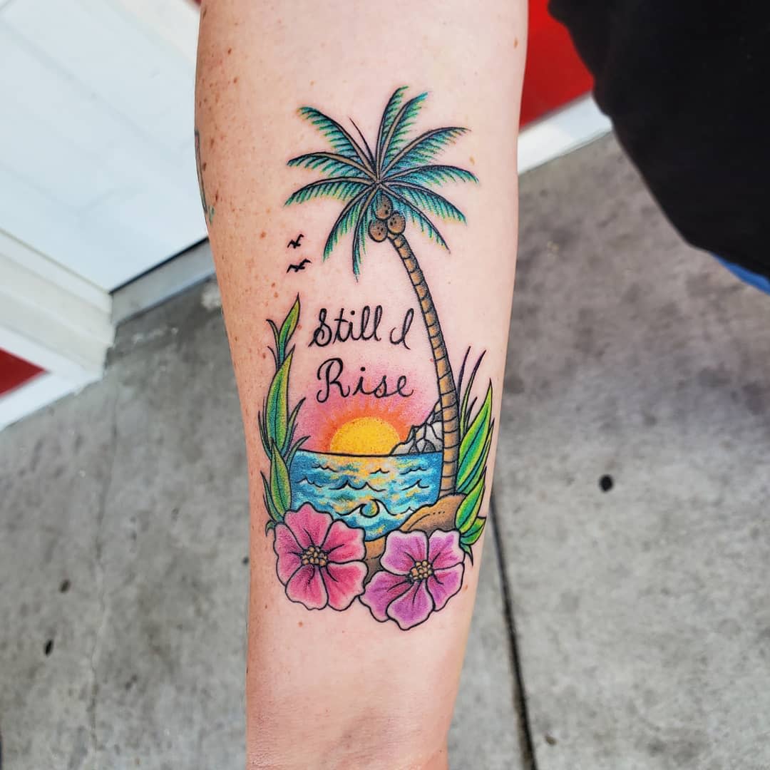 Vibrant tattoo of a beach scene featuring a sunset, palm tree, flowers, and the text "Still I Rise"