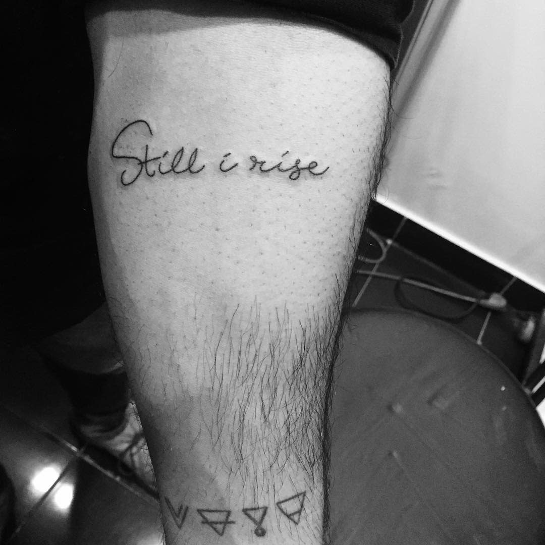 A forearm tattoo reads "Still I rise" in cursive, with geometric symbols below it
