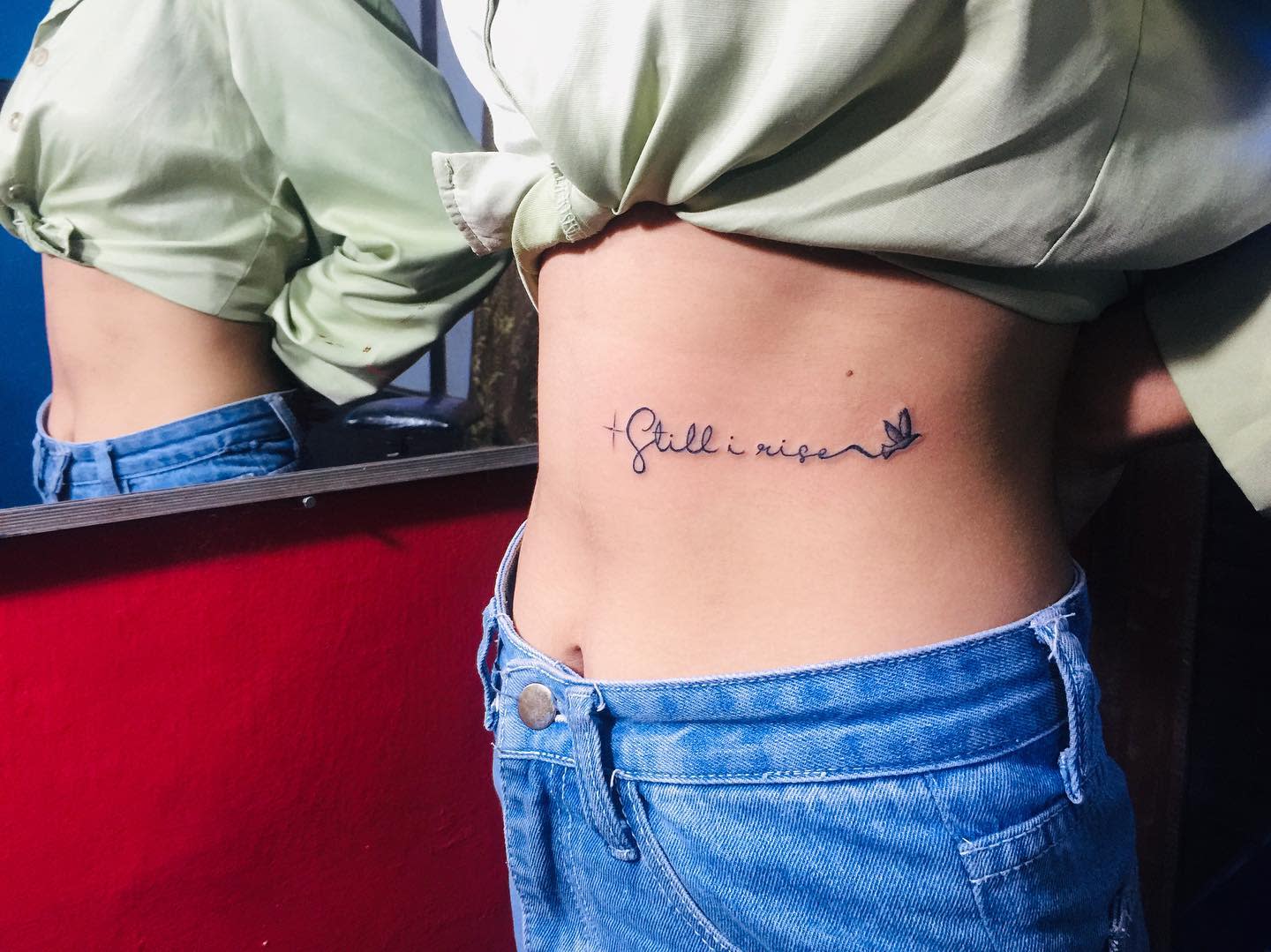 Side tattoo that reads "still I rise" accompanied by a bird