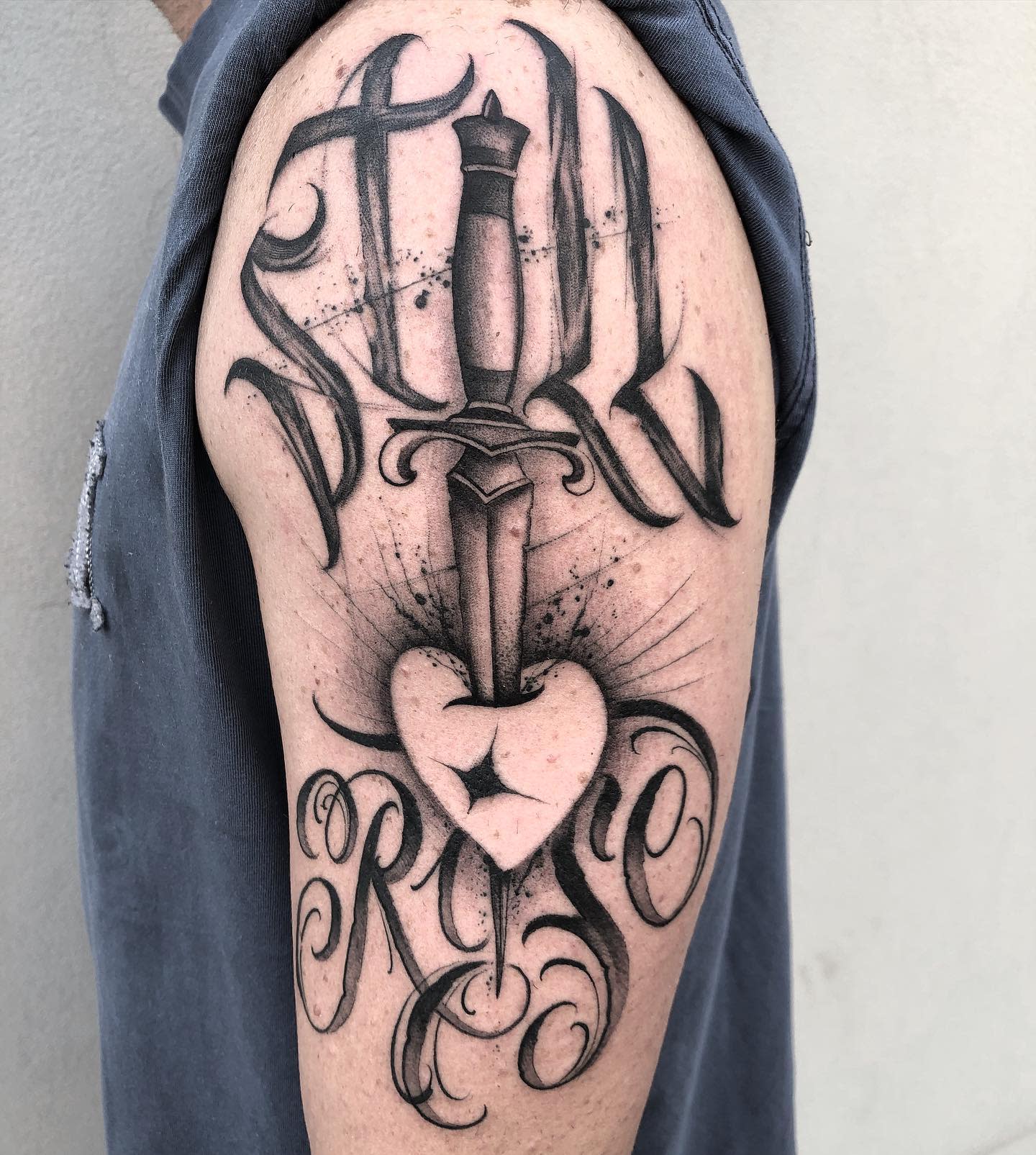 Tattoo of a dagger through a heart with "Still Rise" text on an upper arm