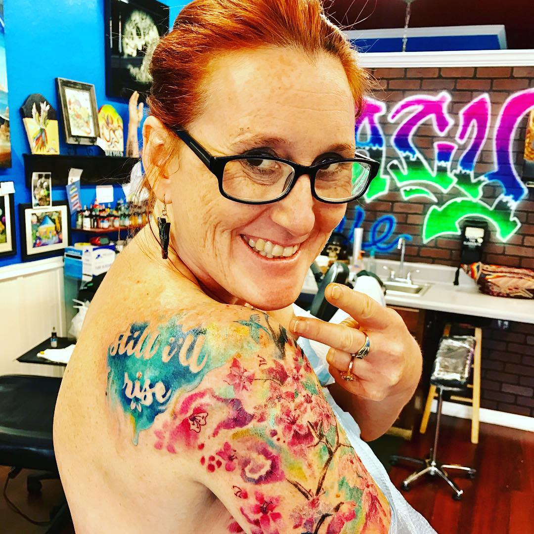 Colorful shoulder tattoo reading "still, I rise" 