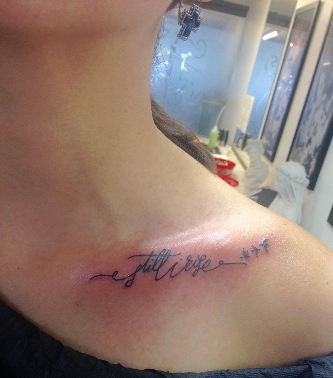 Close-up of a collarbone tattoo reading "still I rise" with small, flying birds next to the text