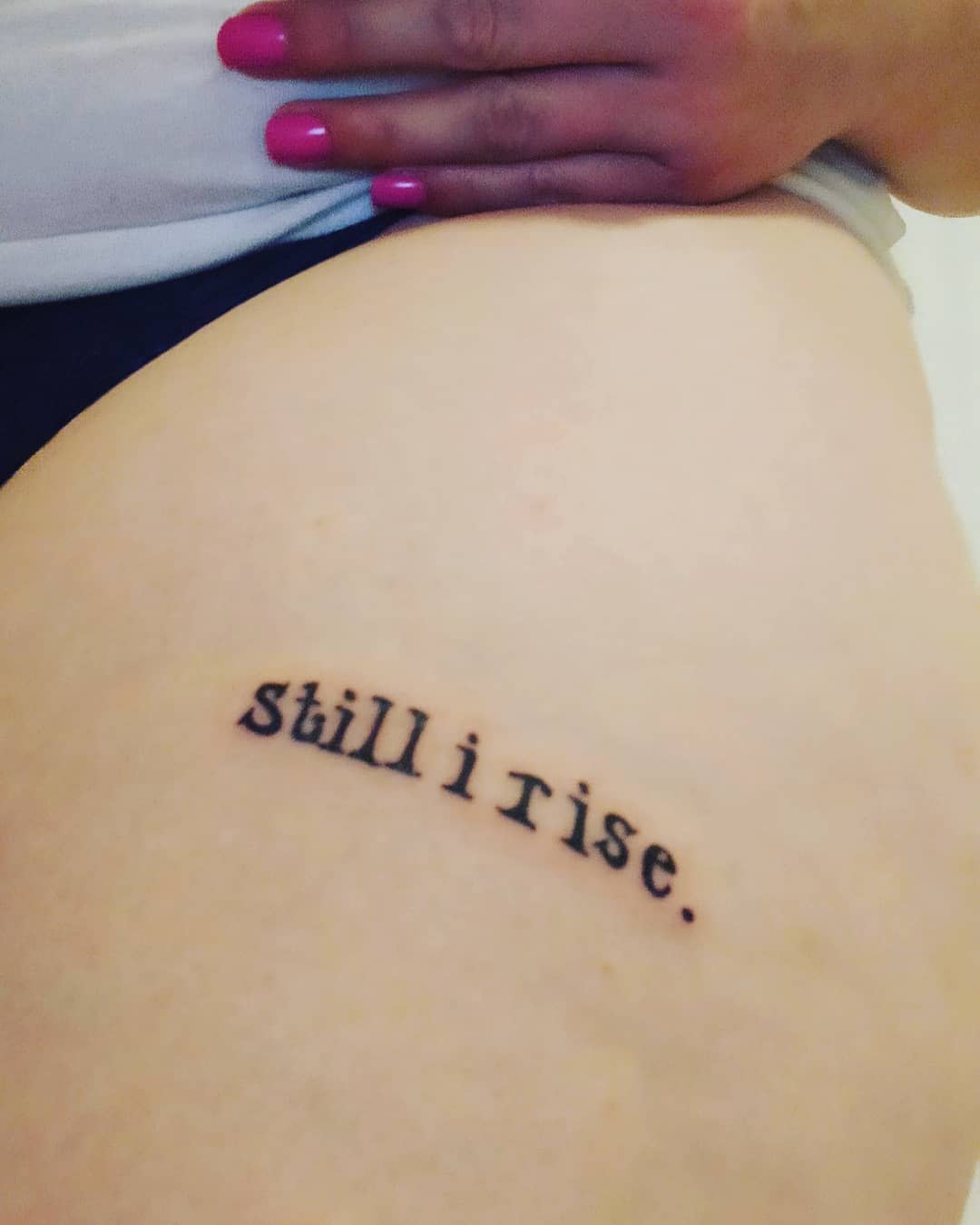 Tattoo on thigh reading "still i rise" in typewriter font