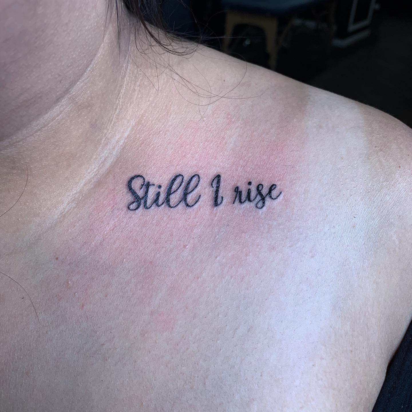 Close-up of a chest tattoo reading "Still I rise" in cursive script