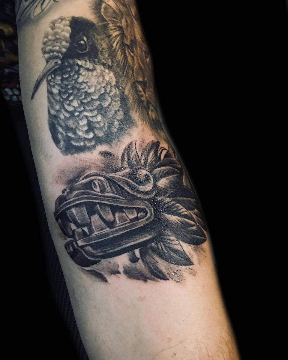 Realistic forearm tattoo of Quetzalcoatl's stone head paired with a detailed bird design