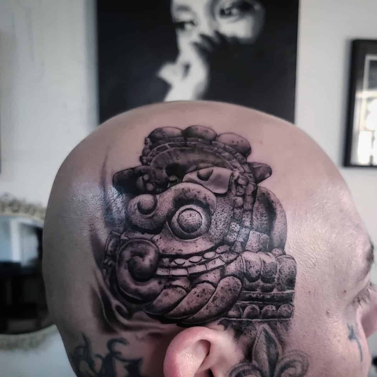 Head tattoo of a stone-carved Quetzalcoatl featuring bold shading and intricate details