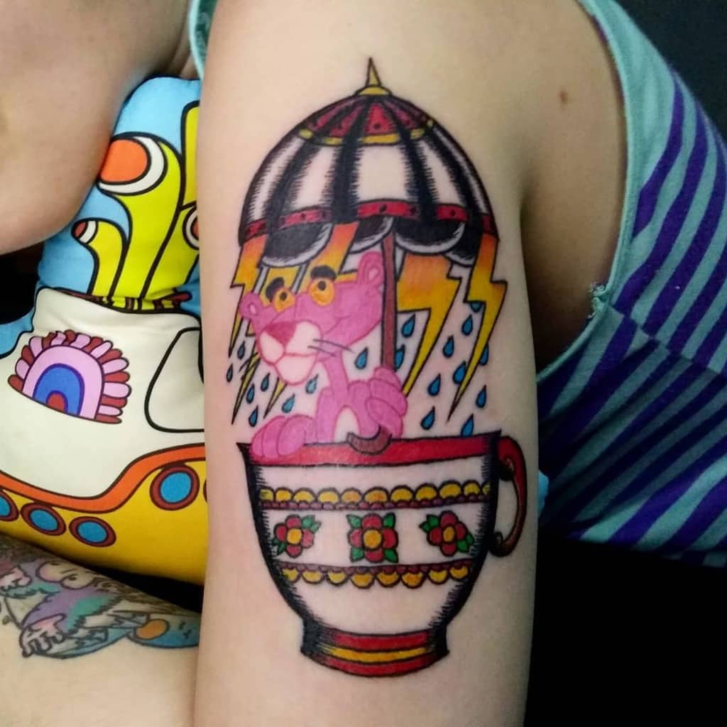 Colorful tattoo of a cartoon pink panther in a floral teacup, under an umbrella with rain, cloud and lightning
