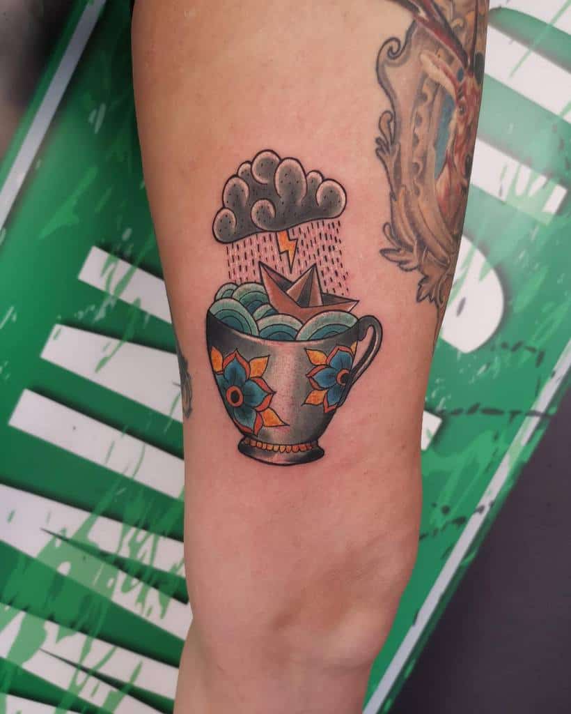 Colorful tattoo of a stormy floral teacup with waves, a thundercloud, lightning, and an origami boat