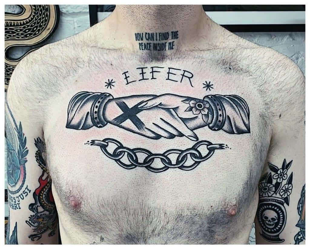 Bold black ink tattoo featuring a handshake with a straight edge 'X,' a flower, two asterisks, the word 'LIFER,' and a broken chain