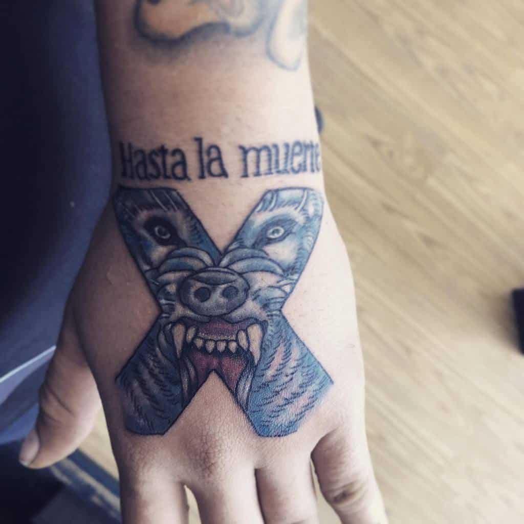 Hand tattoo featuring a bold straight edge 'X' with a snarling wolf face inside, paired with the phrase 'Hasta la muerte'