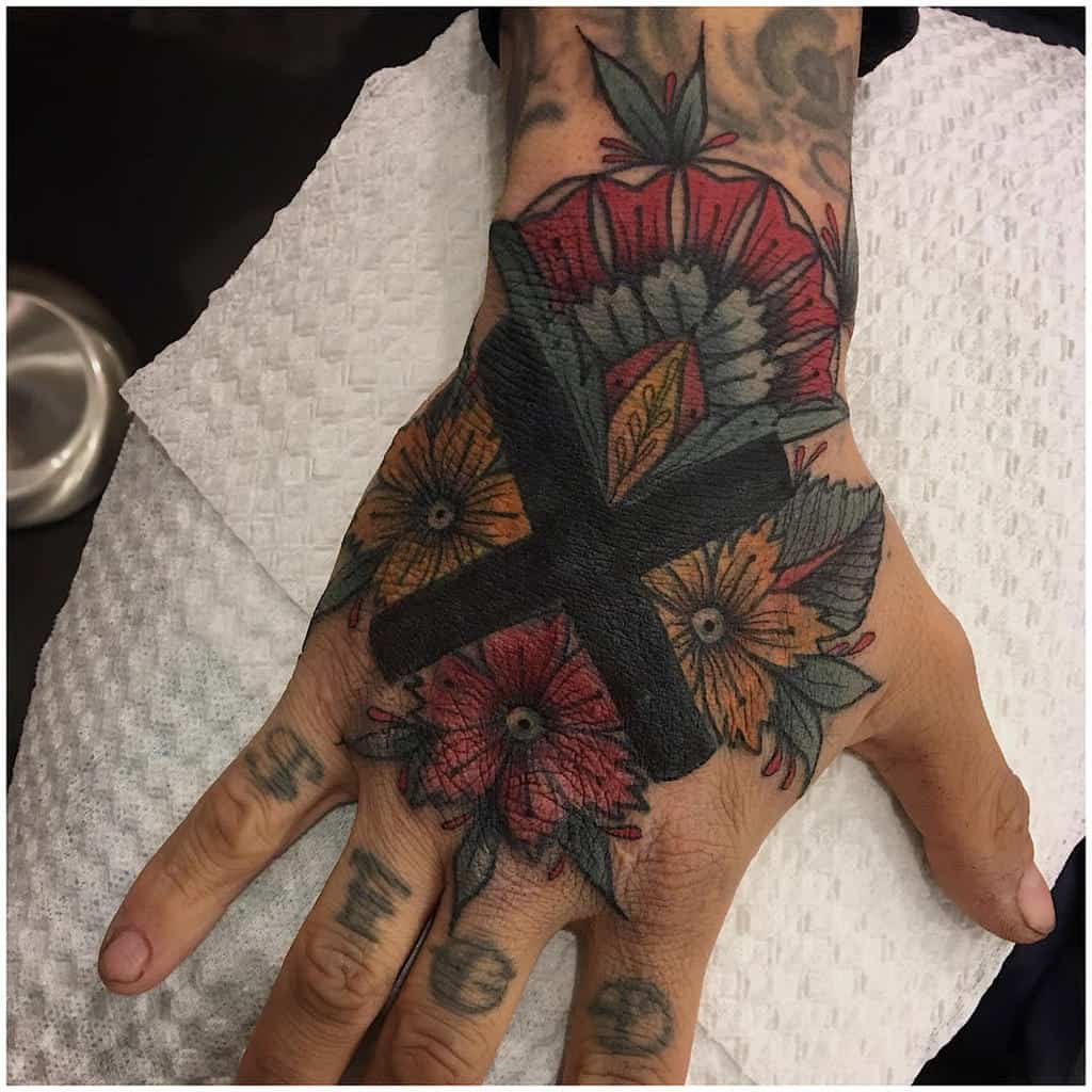 Bold hand tattoo featuring a large black straight edge 'X' over vibrant floral designs