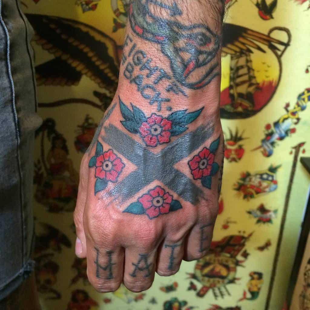 Traditional-style hand tattoo featuring a bold black Straight Edge 'X' adorned with red flowers and green leaves
