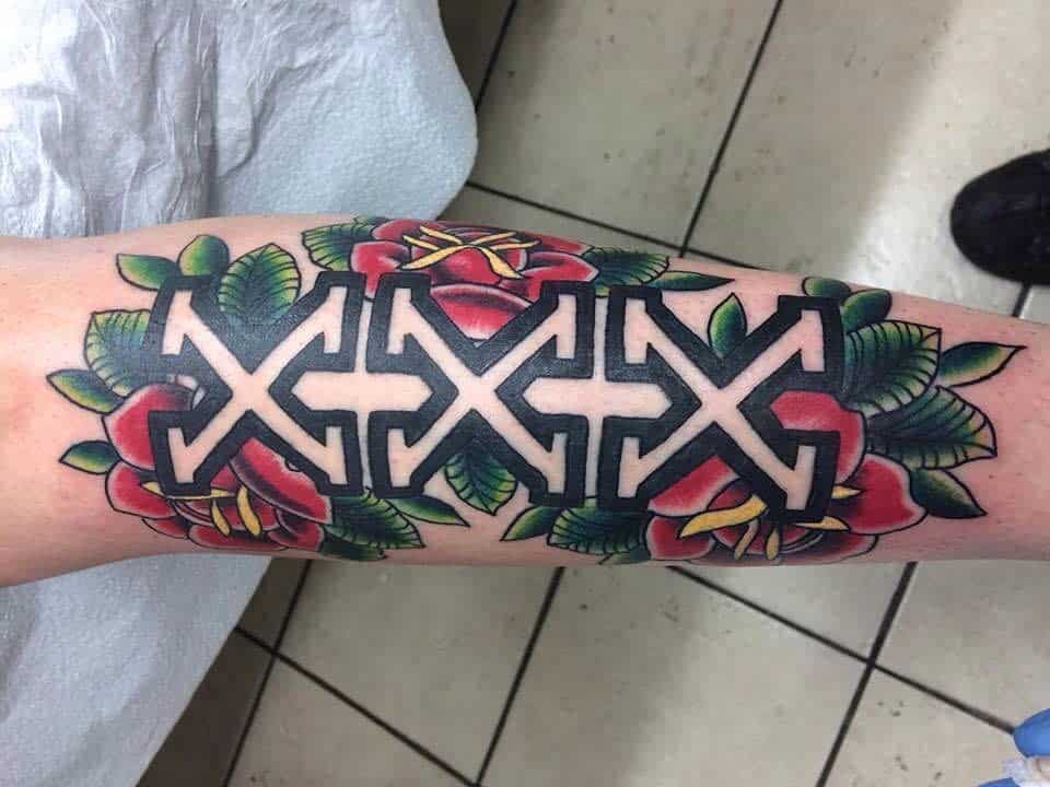 Bold tattoo featuring a black and white 'XXX' straight edge design surrounded by vibrant red roses and green leaves