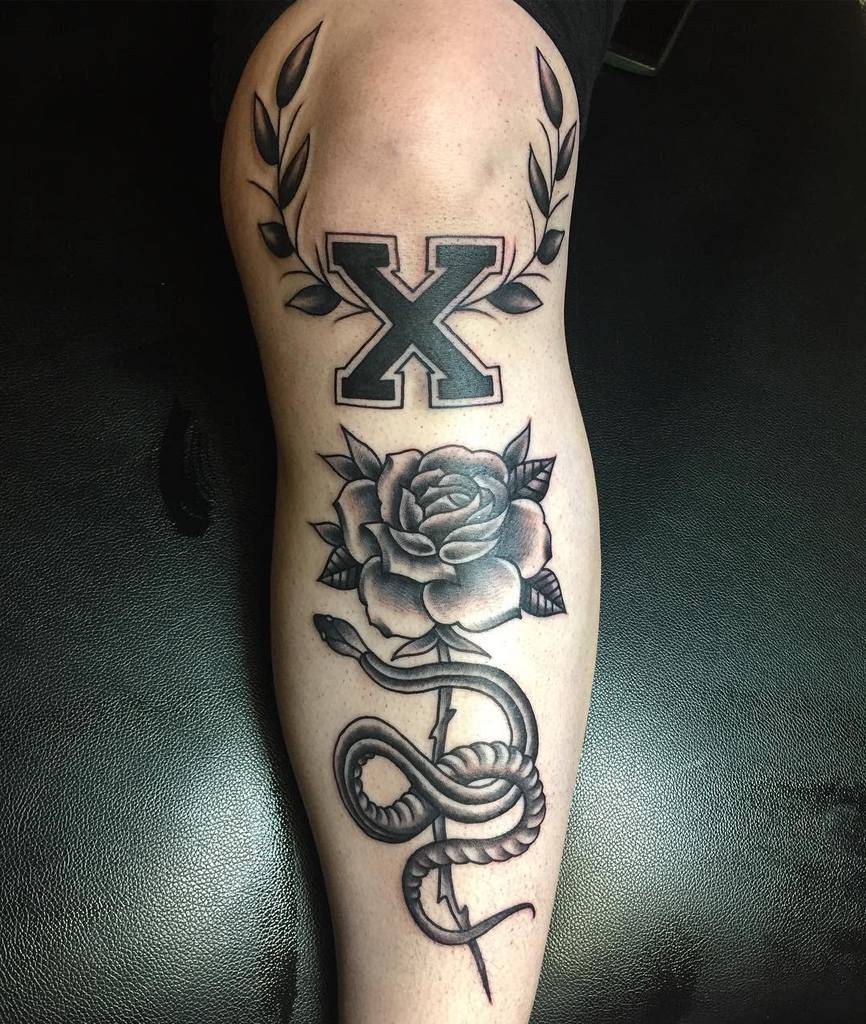 Black and grey straight edge tattoo with a bold 'X' framed by laurel leaves, a detailed rose, and a coiled snake for a striking design
